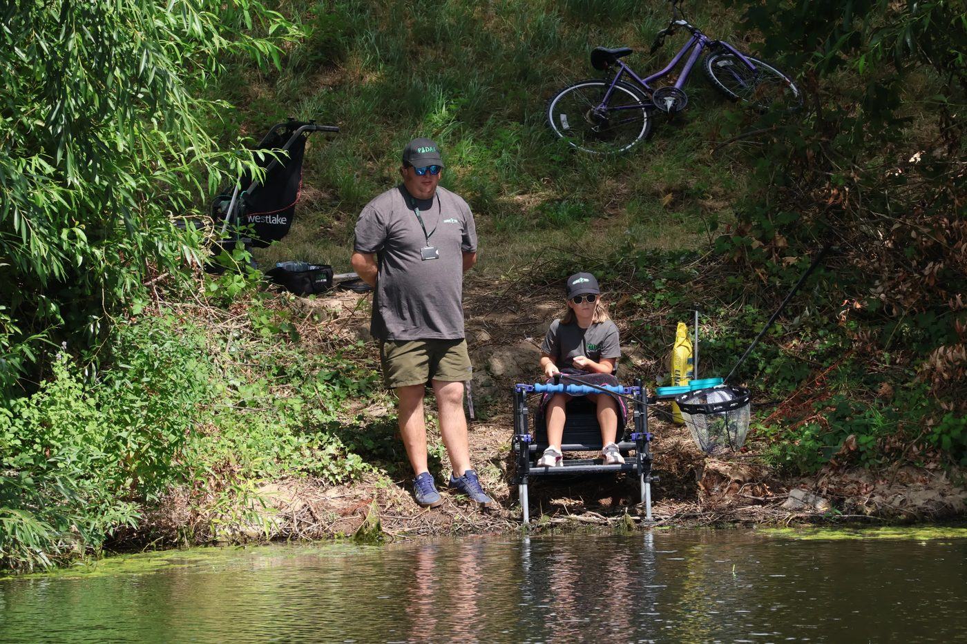 A coach standing back watching a young angler fish, throw line beside the swim