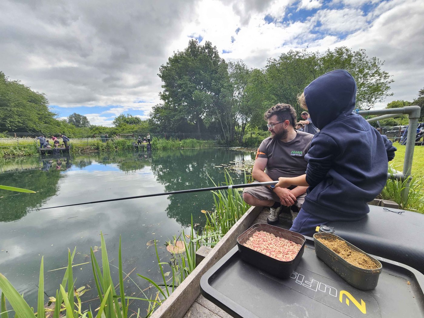 A coach and child fishing a pond on an overcast day