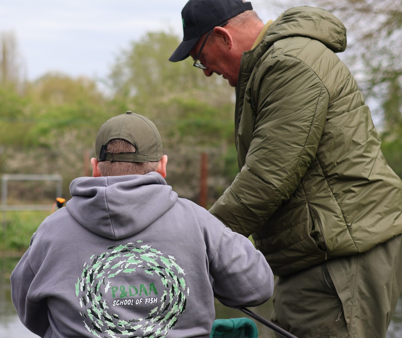 A coach helping a young angler in a School Of Fish hoodie