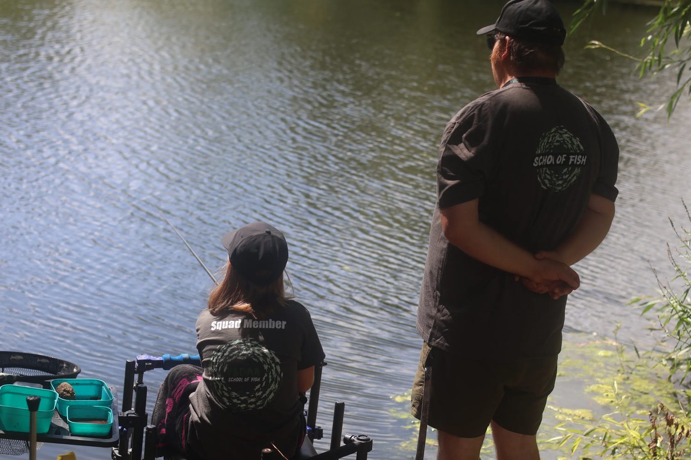 A coach watching over a Squad member fishing in the sunshine